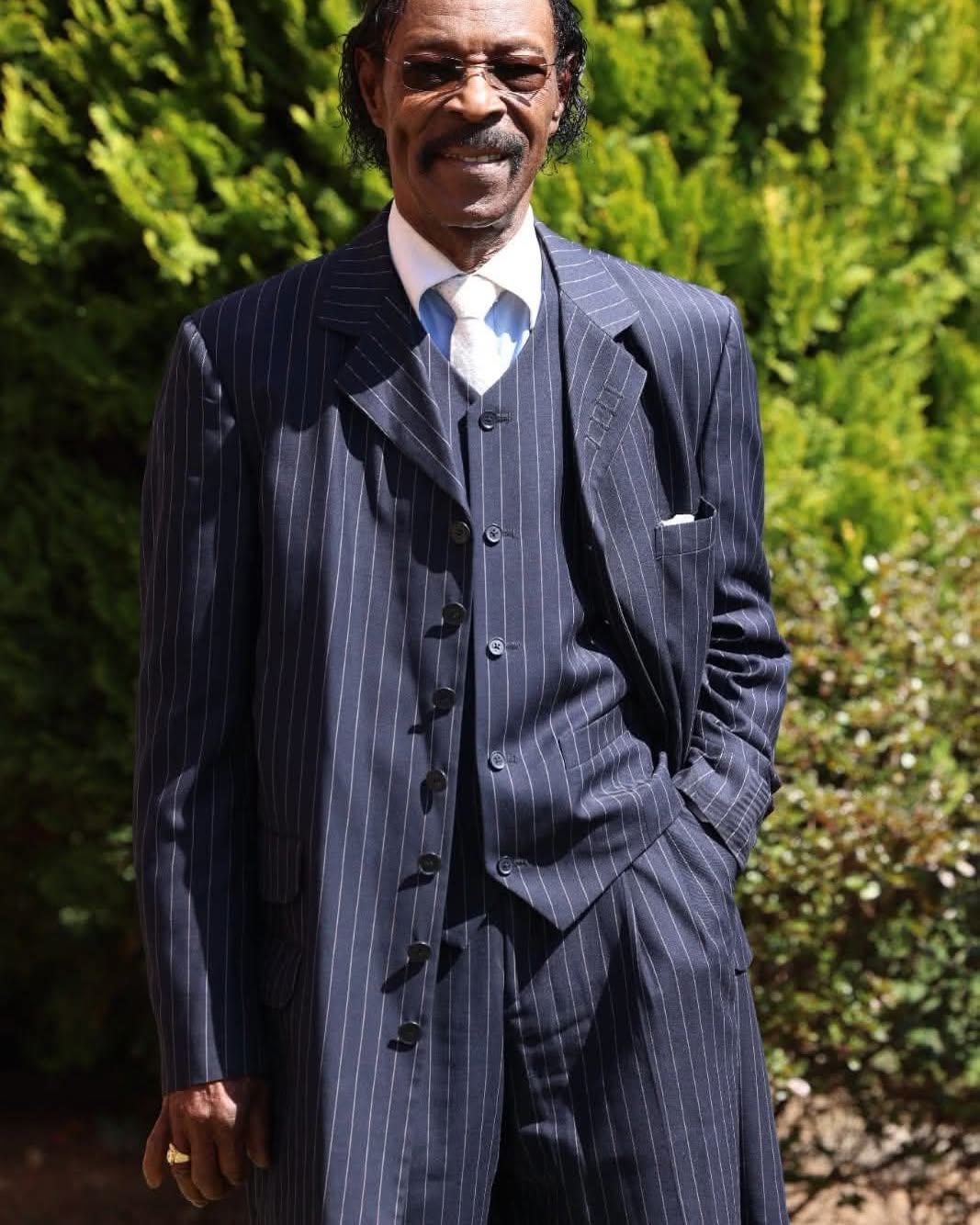 Roman Paul standing outdoors in a navy pinstripe suit